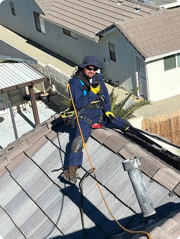 Fieldtech pest control technician in full safety harness and PPE working on a steep residential rooftop performing bird control service in Apple Valley CA